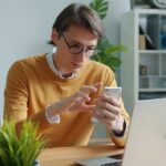Joven usa su celular frente a un computador portátil