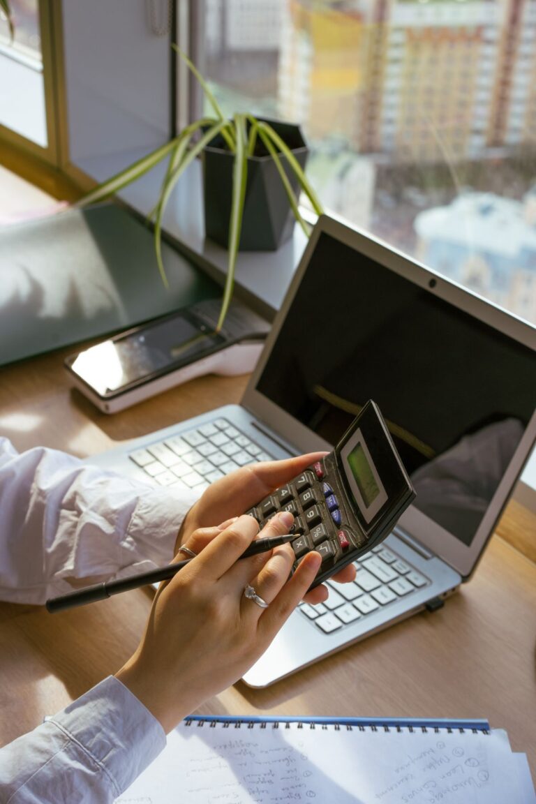 Persona hace cálculos con calculadora y portátil en su escritorio