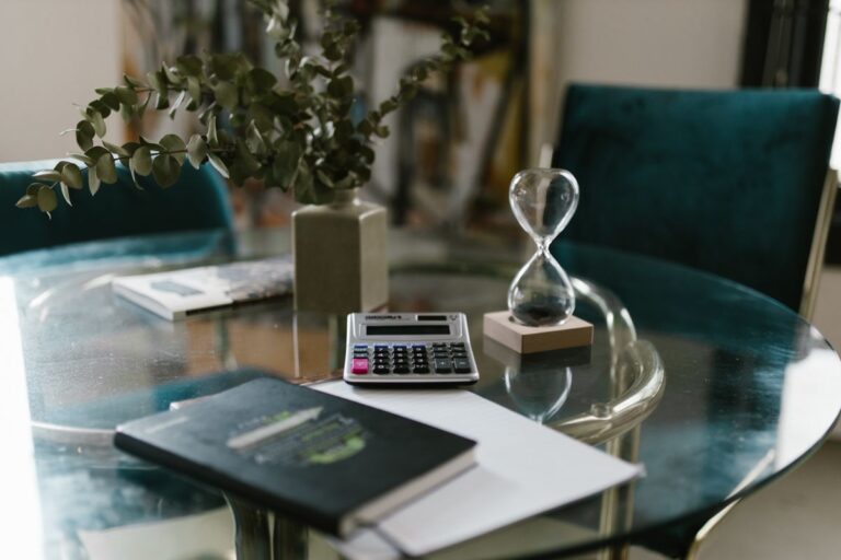 Calculadora, libreta y reloj de arena sobre una mesa de vidrio