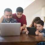 Padre con sus hijos revisando un computador portátil en casa