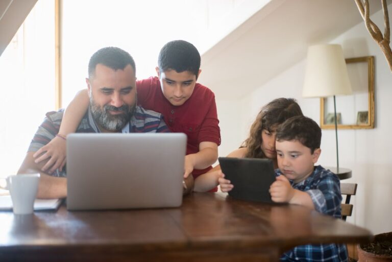 Padre con sus hijos revisando un computador portátil en casa