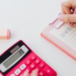 Persona escribiendo en un papel junto a una calculadora