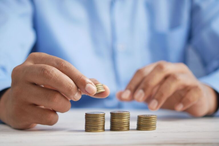 Manos apilando monedas doradas sobre una mesa