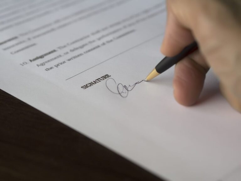 Mano firmando un contrato con bolígrafo sobre un escritorio de madera