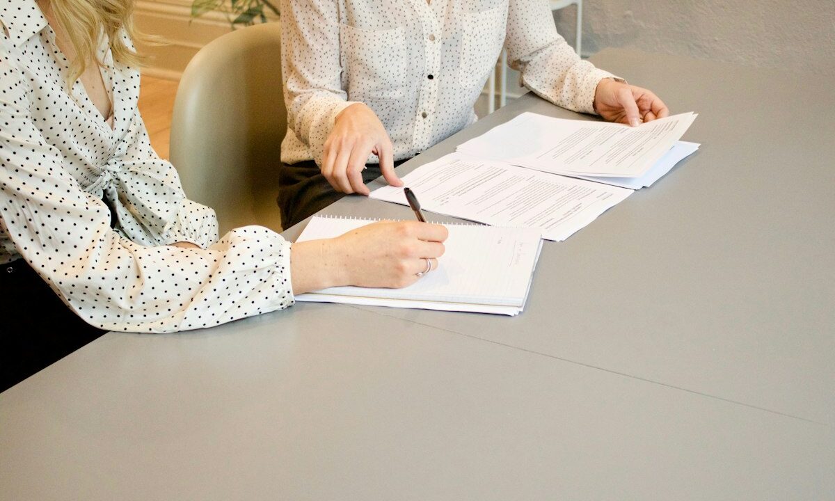 Dos mujeres revisan y firman documentos sobre una mesa