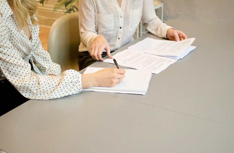 Dos mujeres revisan y firman documentos sobre una mesa