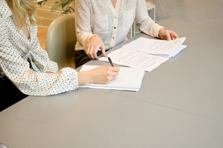 Dos mujeres revisan y firman documentos sobre una mesa