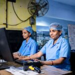 Trabajadoras con uniforme azul en los escritorios de una planta industrial