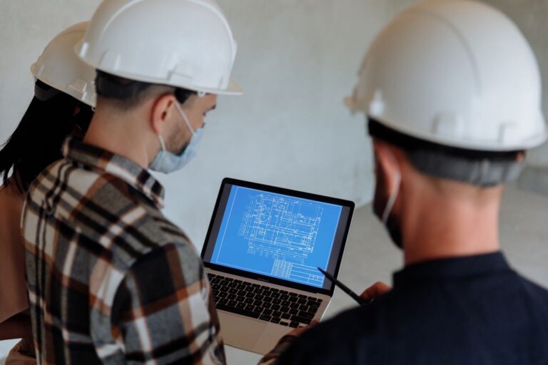 Ingenieros con casco revisan un plano de construcción en un portátil