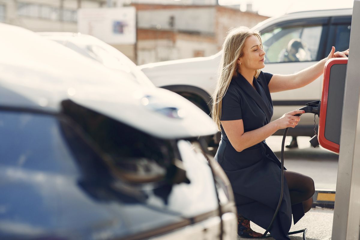 Concepto 018050 del 25-09-2026. Impuesto nacional al consumo. Vehículos híbridos frente a la exclusión de los vehículos eléctricos. 2 Mujer carga un vehículo eléctrico en una estación de la ciudad