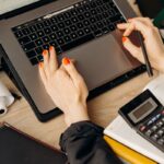 Manos de una contadora trabajando en un computador portátil con una calculadora sobre el escritorio