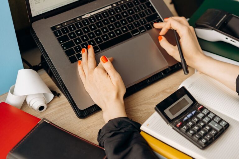 Manos de una contadora trabajando en un computador portátil con una calculadora sobre el escritorio