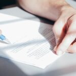 Concepto 014172 del 06-08-2026. Procedimiento. Certificado de existencia y representación legal para interponer el recurso de reconsideración en nombre de una persona jurídica. Manos firmando un documento con un bolígrafo azul sobre un escritorio