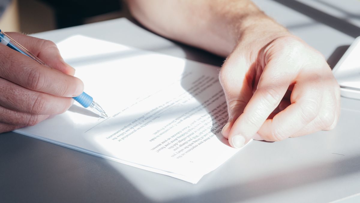 Manos firmando un documento con un bolígrafo azul sobre un escritorio