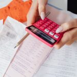 Manos usando una calculadora roja entre documentos y recibos de pago