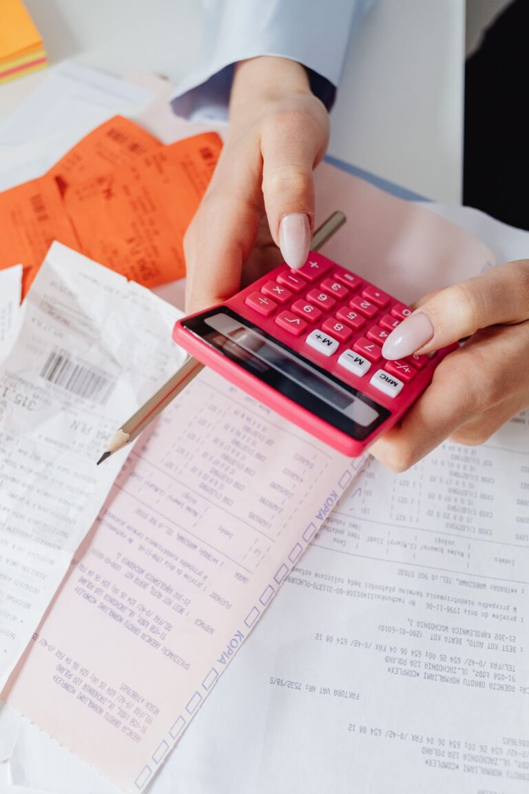 Manos usando una calculadora roja entre documentos y recibos de pago
