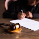 Juez firma documentos en su escritorio junto a un mazo