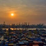 Puerto con contenedores apilados y grúas al atardecer