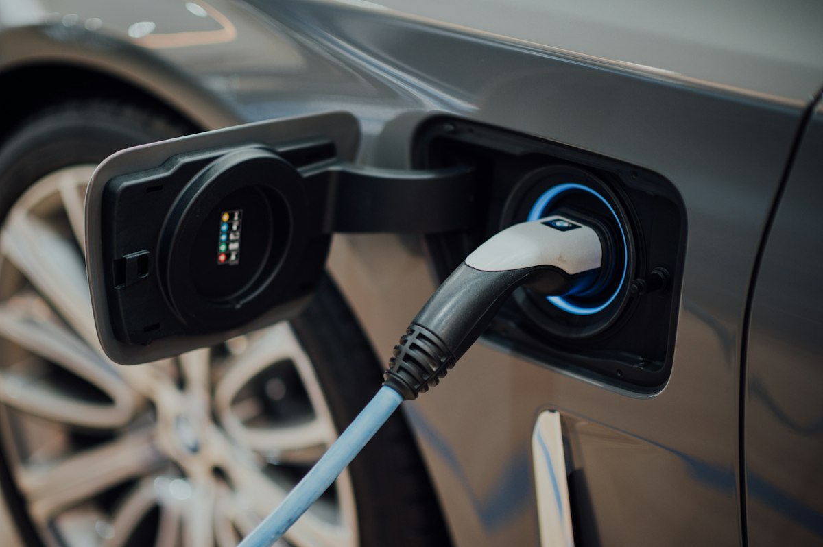 Comunicado de prensa DIAN 127 del 01-10-2026. IVA. Devoluciones por compra de vehículos híbridos y eléctricos. 1 Cable de carga conectado a un vehículo eléctrico